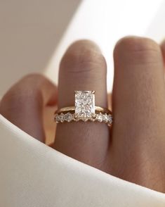 a woman's hand with a diamond ring on top of her finger and white cloth in the background