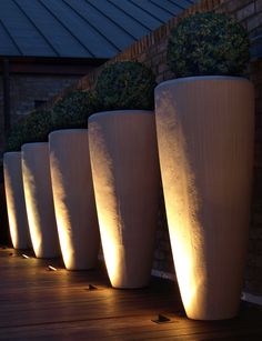 five large white vases are lit up on a deck at night with plants in the background