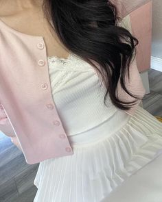 a woman with long black hair wearing a white dress and pink cardigan over her shoulder