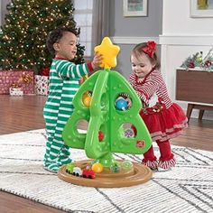 two children in pajamas playing with a christmas tree toy on the floor next to a christmas tree