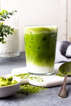 a green drink is sitting on a table next to two spoons