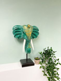 an elephant head on top of a shelf next to a potted plant and green wall