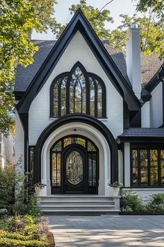 a large white house with black trim and arched glass windows on the front door is surrounded by greenery