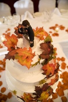 a wedding cake decorated with fall leaves and figurines on the top tiers