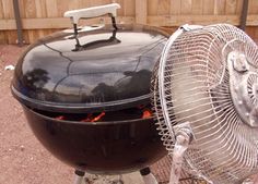 an outdoor bbq grill with a fan on it's side in front of a fence