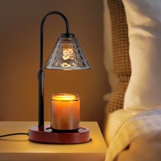 a lit candle sits on a table next to a night stand with a lamp in it