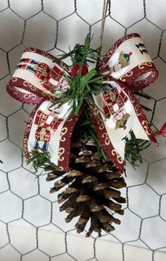 a pine cone ornament hanging on a chicken wire fence with red and white ribbon