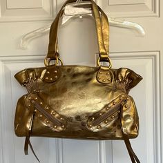 Nwot Gold Color With Brown Lining And Snap Closures. Has Gathering Effect On Each Side. Nice Large Size Bag. It Has A Sheer Similar To A Foil Look. 2 Zipper Small Pockets On Front With Tassels. Gold Tone Hardware. See Photos For Approximate Measurements And Also The Last Photo Shows Several Tiny Spots. I’m Not Sure If In The What It Is. I Saw One On The Other Side. It’s Not Noticeable But I Wanted To Point This Out. Smoke And Pet Free Home. Gold Satchel Shoulder Bag With Large Capacity, Gold Satchel With Metal Hardware For Travel, Gold Large Capacity Satchel Shoulder Bag, Gold Shoulder Bag With Large Capacity And Double Handle, Gold Large Capacity Satchel, Gold Shoulder Bag With Metal Hardware, Handheld Gold Shoulder Bag, Gold Leather Shoulder Bag Large Capacity, Large Capacity Gold Satchel