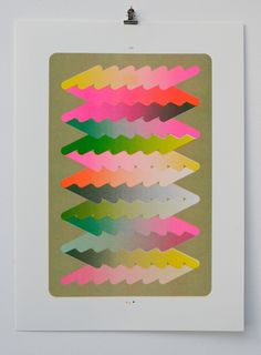 an art piece is hanging on the wall in front of a white frame with pink, yellow and green shapes