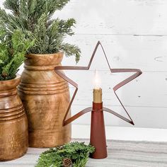 a wooden star next to two vases filled with greenery and a lit candle