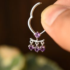 Amethyst has been a symbol of royalty for centuries. Its deep purple color is associated with luxury, wealth, and power and is believed to have healing and protective powers. This unique septum clicker is crafted in solid 14k or 18k gold, with dangling Amethysts, for the subtle charm. It is a stunning addition to our collection and will be for your setup too. The hinged click mechanism makes it secure.  VERTICAL INNER LENGTH OF HOOP: 8mm (ALL IMAGES) *  Gold: 14k / 18k Solid Gold  *  Gold Colour Elegant Pierced Septum Ring For Gift, Elegant Pierced Septum Ring As Gift, Elegant Septum Ring As A Gift, Elegant Septum Ring Gift, Purple Amethyst Hoop Jewelry, Elegant Sterling Silver Hoop Septum Ring, Dainty Amethyst Jewelry In White Gold, Dainty Amethyst White Gold Jewelry, Dainty White Gold Amethyst Jewelry