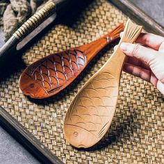 a person holding a wooden spoon next to a fish shaped paddle on a woven surface