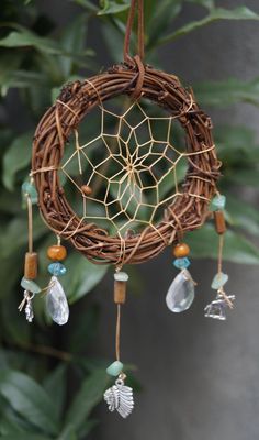 a brown wicker dream catcher hanging from a tree branch with beads and leaves on it