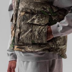 a man wearing a camouflage vest with his hands on his hip and the back of his body