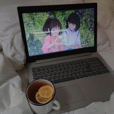 an open laptop computer sitting on top of a bed next to a cup of coffee