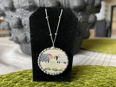 a necklace with two sheep on it is sitting on a black display stand in front of a rock