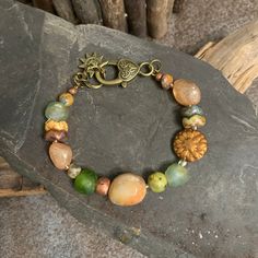 "Summertime" - The bracelet features peach silver coated quartz gemstone that glimmer like the hot sky of a late summer afternoon.  The deep greens of African glass and agate rounds are reminiscent of the thick park grass with the wavey floral discs being the prolific perennial summer flowers with the rust colored Dahlia coin as the grand centerpiecre of the gardens. A large jade nugget pulls the landscape together.  A beautiful bronze heart lobster claw closure completes the summertime cirlce.  As Ella Fitzgerald sings while Louis Armstrong trumpets, "Summertime, and the living is easy". Grab a pcinic basket, a blanket and a good book and look will be complete. Size 7.50. I can adjust this to fit up to to 8.5 inches.  Please let me know your desired size. I begin each piece by hand select Bohemian Amber Beaded Bracelets Hand-strung, Bohemian Agate Beaded Bracelets, Orange Bohemian Beaded Bracelets, Handmade Orange Agate Bracelets, Orange Bohemian Bracelets For Festivals, Handmade Orange Agate Bracelet, Artisan Orange Bracelets As Gift, Bohemian Orange Bracelets For Festivals, Bohemian Orange Hand-strung Bracelets