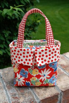 a red and white polka dot purse sitting on top of a brick wall next to green grass