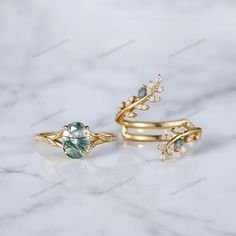 two gold rings with green and white stones on them, sitting on a marble surface