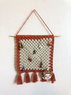 a crocheted wall hanging with buttons and tassels on a white wall