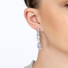 Step into a world of glamour with the Crawford Drop Earrings in Silver White. Exquisitely fashioned  and resplendent with dazzling simulated diamonds, these earrings exude an Art Deco charm that’s both vintage and timeless.  The elegant drop design features five rectangular settings. Each setting is graced with a unique arrangement of gemstones, crowned by a single radiant simulated diamond at the bottom, encircled by a stunning array of baguette-cut stones.   These earrings are designed for bot Luxury Baguette Diamond Earrings For Formal Events, Luxury Silver Baguette Cut Diamond Earrings, Luxury White Cubic Zirconia Linear Earrings, Glamorous Diamond White Brilliant Cut Earrings, Luxury Brilliant Cut Diamond Earrings For Evening, Luxury Crystal Earrings For Evening, Luxury Bridal Earrings With Sparkling Stones, Luxury Diamond Baguette Cut Earrings, Luxury Sterling Silver Linear Earrings For Party