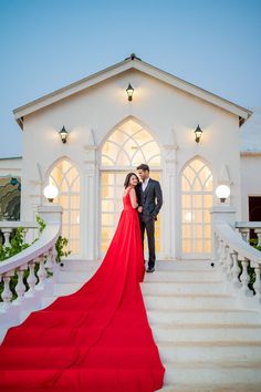 a man and woman standing on steps in front of a white building with red carpet