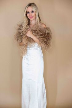 a woman in a white dress and fur shawl posing for the camera with her hands on her hips