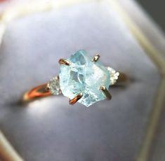 Raw gemstone ring with accented diamonds. Please select the main stone from the drop down menu.  𝗗𝗘𝗧𝗔𝗜𝗟𝗦 𝗠𝗔𝗜𝗡 𝗦𝗧𝗢𝗡𝗘 𝗚𝗲𝗺𝘀𝘁𝗼𝗻𝗲: Aquamarine 𝗖𝗼𝗹𝗼𝗿: Blue 𝗦𝗵𝗮𝗽𝗲: Other 𝗖𝘂𝘁: Raw 𝗠𝗲𝗮𝘀𝘂𝗿𝗲𝗺𝗲𝗻𝘁: 9x8 mm 𝗦𝗜𝗗𝗘 𝗦𝗧𝗢𝗡𝗘𝗦 𝗗𝗶𝗮𝗺𝗼𝗻𝗱, round, brilliant cut, 3.00 mm (approx. 0.22 ct) (2) 𝗗𝗶𝗮𝗺𝗼𝗻𝗱 𝗾𝘂𝗮𝗹𝗶𝘁𝘆: Clarity grade VS, color grade F-G, conflict-free 𝗕𝗔𝗡𝗗 𝗦𝘁𝘆𝗹𝗲: 3-stone 𝗠𝗮𝘁𝗲𝗿𝗶𝗮𝗹: 14k gold (yellow, white, rose), 18k gold (ye Trillion Cut Diamond Jewelry For Proposal, Diamond Jewelry With Accent Stones For Proposal, Cubic Zirconia Jewelry With Side Stones For Gift, Exquisite Ethical Diamond Ring, Fine Jewelry Ring With Side Stones, Fine Jewelry With Side Stones For Anniversary, Diamond Promise Jewelry With Side Stones, Promise Jewelry With Side Stones, Aquamarine Diamond Ring With Accent Stones