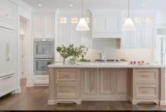 a large kitchen with white cabinets and wooden flooring, along with an island in the middle