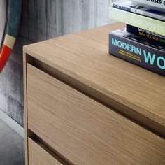 a stack of books sitting on top of a wooden dresser next to a surfboard