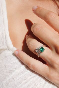 a woman's hand with an emerald and diamond ring on her left hand, wearing a white sweater