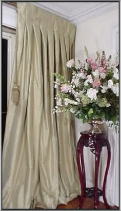 a vase filled with flowers sitting next to a window covered in drapes and curtains