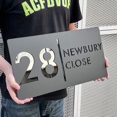 a man holding up a sign that says newbury close to the number twenty eight