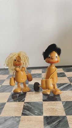 two wooden dolls are standing on a checkered floor