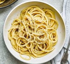 a white bowl filled with pasta on top of a table next to a fork and spoon