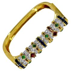 A unique, modern, hinged cuff bracelet, with a slightly squared off design. This colorful piece tapers in width from just under half an inch at the top, down to 1/4 of an inch at the base. Crafted in 18K yellow gold, the top has the appearance of a cylinder of diamonds accented by bands of emerald, ruby, and sapphire. The outer walls of this piece feature a detailed pattern resembling scales or cobblestones. There are a total of 64 round brilliant cut diamonds weighing a combined weight of approximately 2.25ct of overall G color and VS2 clarity. The colored stones added to the backdrop of diamonds weigh a total of approximately 5.75ct. Stamped 750 and 18K. Inside circumference measures 7 inches. Gross weight 57.6 grams. Ruby And Sapphire, Colored Stones, Ruby Sapphire, Top Down, Bracelets And Charms, Round Brilliant Cut Diamond, Vintage Watches, Round Brilliant, Cuff Bracelet