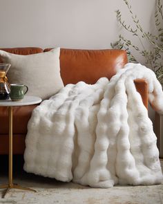 a brown leather couch with a white blanket on it's back next to a coffee table