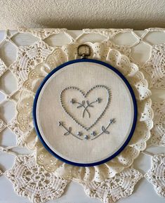 an embroidered heart on a white doily with crocheted lace and blue trim