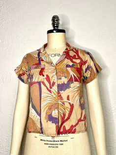 Relax and look cool in this classic vintage 90s Hawaiian collard blouse with an Orchid design in beige, purple, red, green, & white. Showcasing a simple motif of Orchid Flowers. This Hawaiian-made shirt is sewn with two front breast pockets, button up closure, and single stitched short sleeves in a soft cotton fabric. This is an easy Hawaiian or summer shirt choice for just about any day. Measurements: Armpit to armpit: 18 inches Back length: 23 inches Multicolor Retro Print Button-up Top, 90s Style Relaxed Fit Button-up Top, Cotton Tops With Retro Print And Camp Collar, Cotton Top With Retro Print And Camp Collar, Summer Collared Tops With Retro Print, Short Sleeve Cotton Tops With Vintage Print, Multicolor Collared Top With Retro Print, Cotton Vintage Print Short Sleeve Tops, Cotton Short Sleeve Tops With Vintage Print