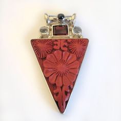 "Cinnabar, with a lovely floral design, has been bezel set in 925 Sterling Silver in this gorgeous bright red pendant.  Cinnabar is a resin that comes from the Laq tree in Asia. Once hardened, skilled artisans carve wonderful patterns in the medium.  This pendant also features a rectangle of Garnet, two rounds of Moonstone and a round of Black Star Diopside adorns the tube bale. The total length of this piece is 1 3/4\" long. Designed by Marianna and Richard and handmade by Balinese Artisans an Red Bohemian Flower Pendant Jewelry, Bohemian Red Flower Pendant Jewelry, Red Cabochon Spiritual Jewelry, Spiritual Red Cabochon Jewelry, Red Sterling Silver Jewelry With Inlay, Artisan Red Carved Jewelry, Red Multi-stone Jewelry Gift, Red Multi-stone Jewelry As Gift, Red Multi-stone Jewelry For Gifts