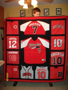 a young boy standing in front of a red and black baseball jersey quilted to the ceiling