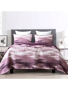 a bed covered in a purple and white comforter next to a night stand with two nightstands