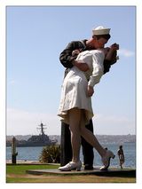 a man and woman are kissing in front of a statue by the water's edge