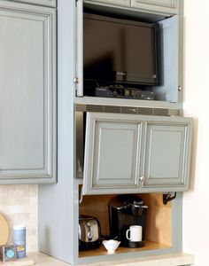 a kitchen with gray cabinets and coffee maker in the cupboards, which is open to reveal an entertainment center