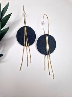 two pairs of black and gold earrings on a white surface with a plant in the background