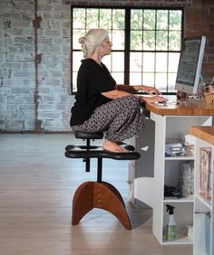 an older woman sitting at a desk with a computer on top of it and looking out the window