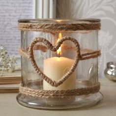 a candle in a glass jar with a heart on the front and rope around it