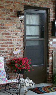 a rocking chair sitting in front of a door with flowers on the porch next to it