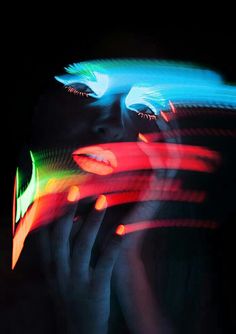 a woman's face is lit up with neon lights and her hands are in front of her face