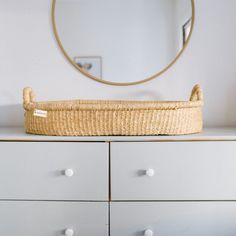 a wicker basket sitting on top of a dresser next to a round mirror above it